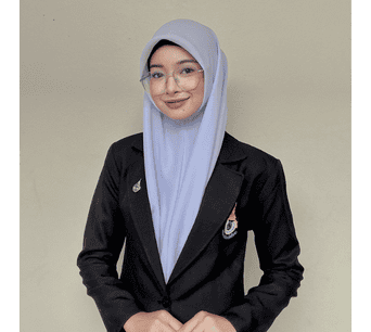 ภาพของนักศึกษาหญิงในชุดเครื่องแบบนักศึกษา สวมผ้าคลุมศีรษะสีฟ้าอ่อน ยืนถ่ายภาพในห้องเรียนหรือสถาบันอิสลามและอาหรับศึกษา มนร.