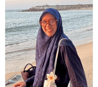 ภาพหญิงนักศึกษาสวมผ้าคลุมฮิญาบสีฟ้าบนชายหาด แสดงความภาคภูมิใจในวัฒนธรรมอิสลามและการศึกษาอาหรับในมหาวิทยาลัยนราธิวาสราชนครินทร์.