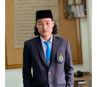 ภาพนักเรียนชายในชุดเครื่องแบบนักเรียนอิสลามและอาหรับศึกษา มนร. ยืนอยู่ในห้องเรียนหรือห้องสมุดของสถาบันอิสลามและอาหรับศึกษา มนร.