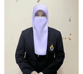 ภาพหญิงนักศึกษาสวมชุดฮิญาบและเสื้อสูทของสถาบันอิสลามและอาหรับศึกษา มนร. ยืนอยู่ในห้องเรียนหรือสำนักงาน แสดงความเป็นมืออาชีพและความภาคภูมิใจในวัฒนธรรมอิสลามและภาษาอาหรับ.